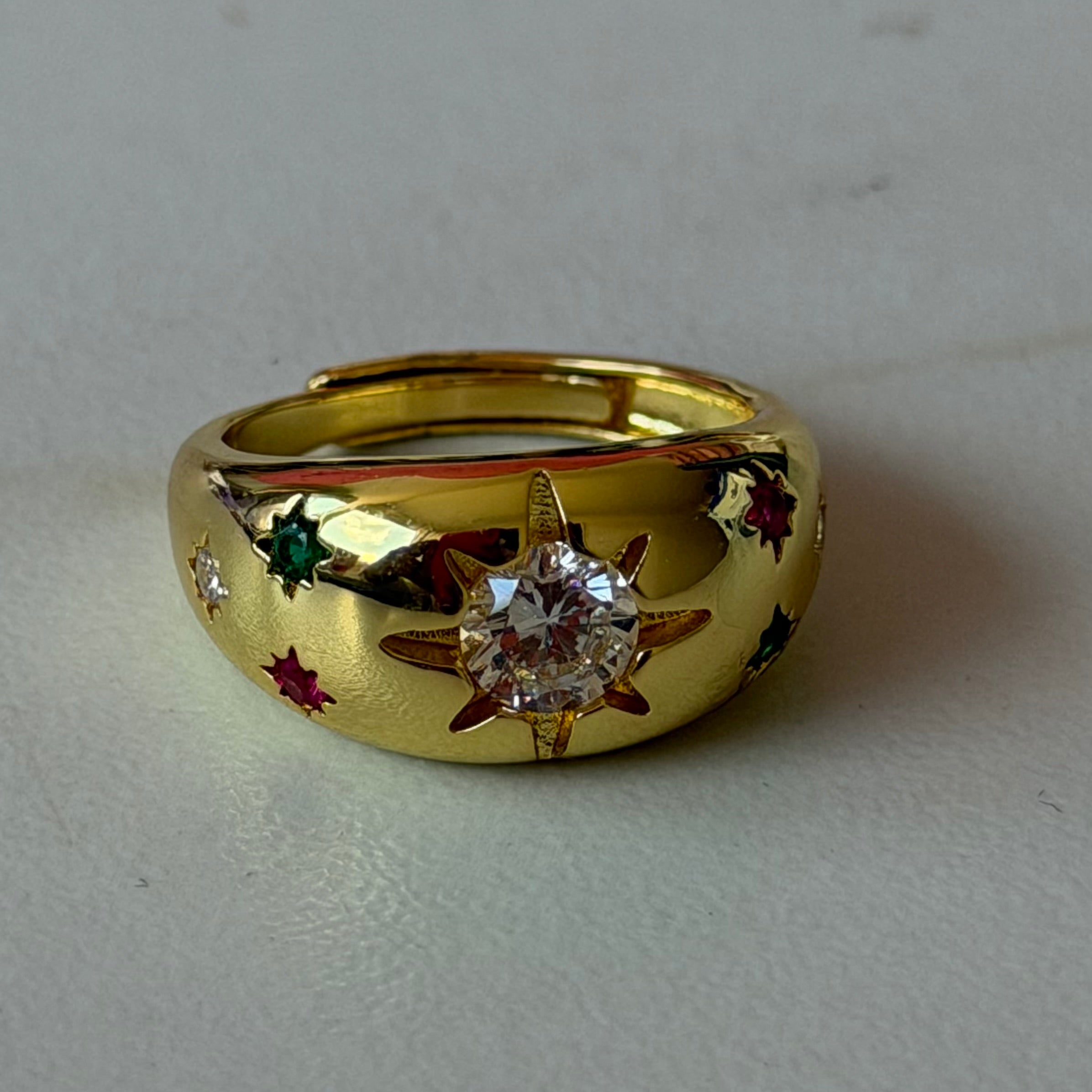 Gold ring with star design and gemstones on a light gray background