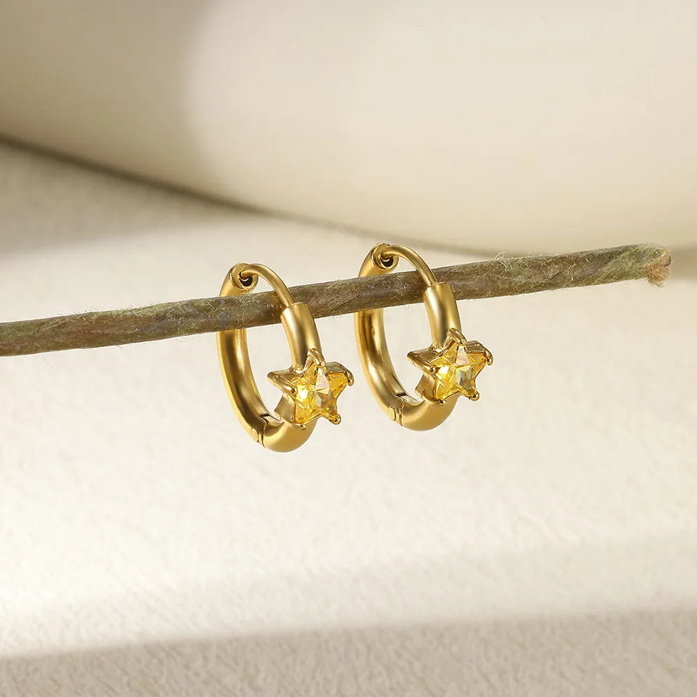 Gold hoop earrings with star-shaped charms on a branch against a neutral background