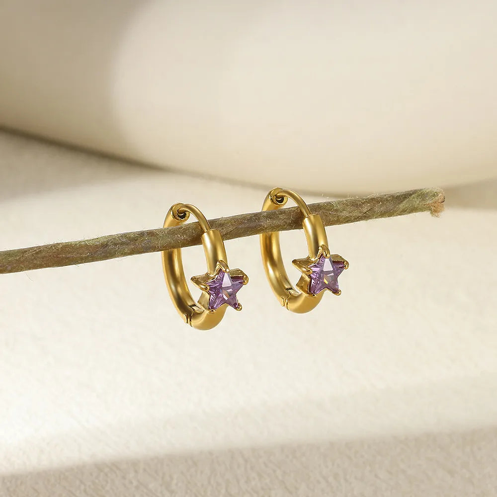 Gold hoop earrings with purple star-shaped stones on a wooden stick.