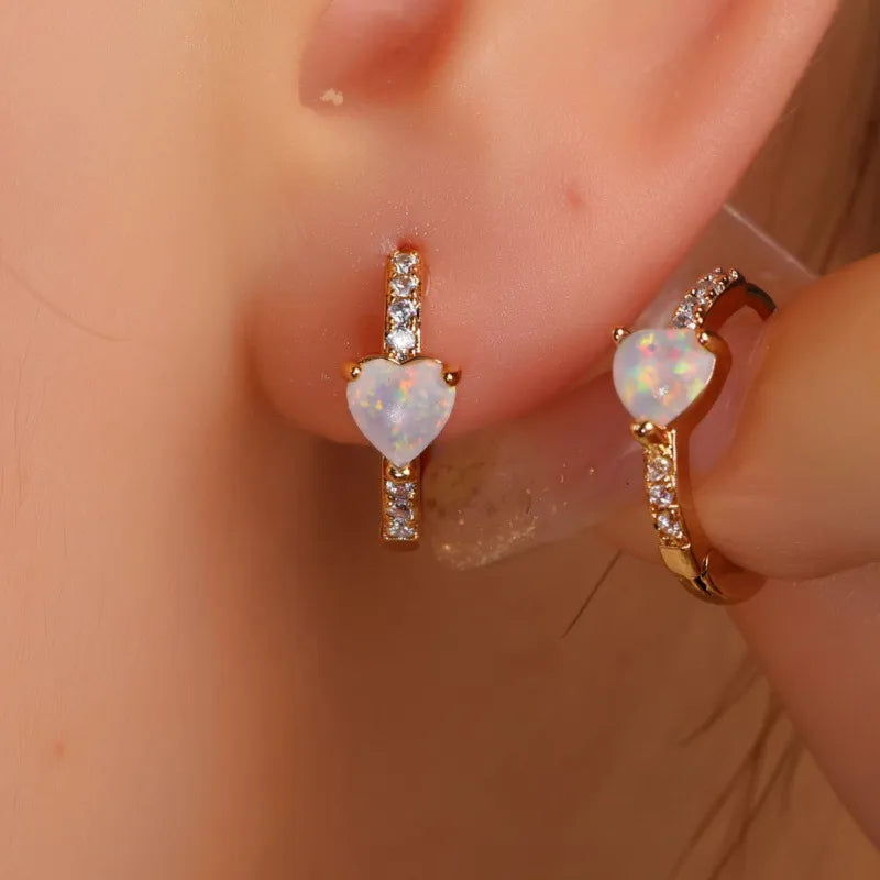 Heart-shaped opal earrings with rose gold setting worn on an ear.