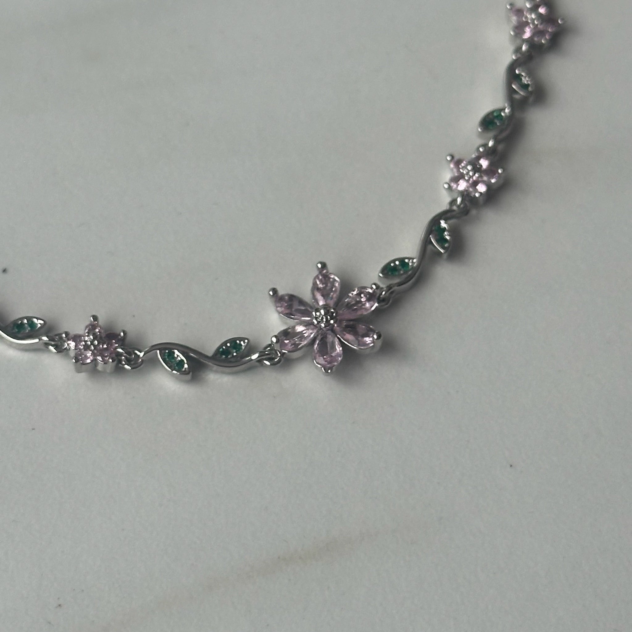 Silver bracelet with pink and green gemstones on a light gray background