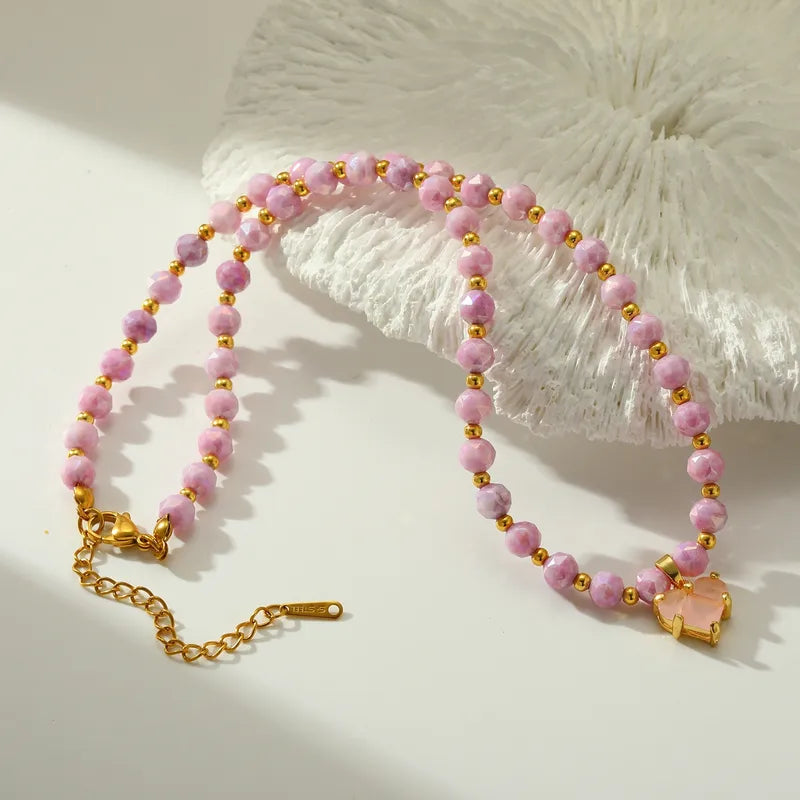 Necklace with pink beads and a heart-shaped charm on a textured white surface