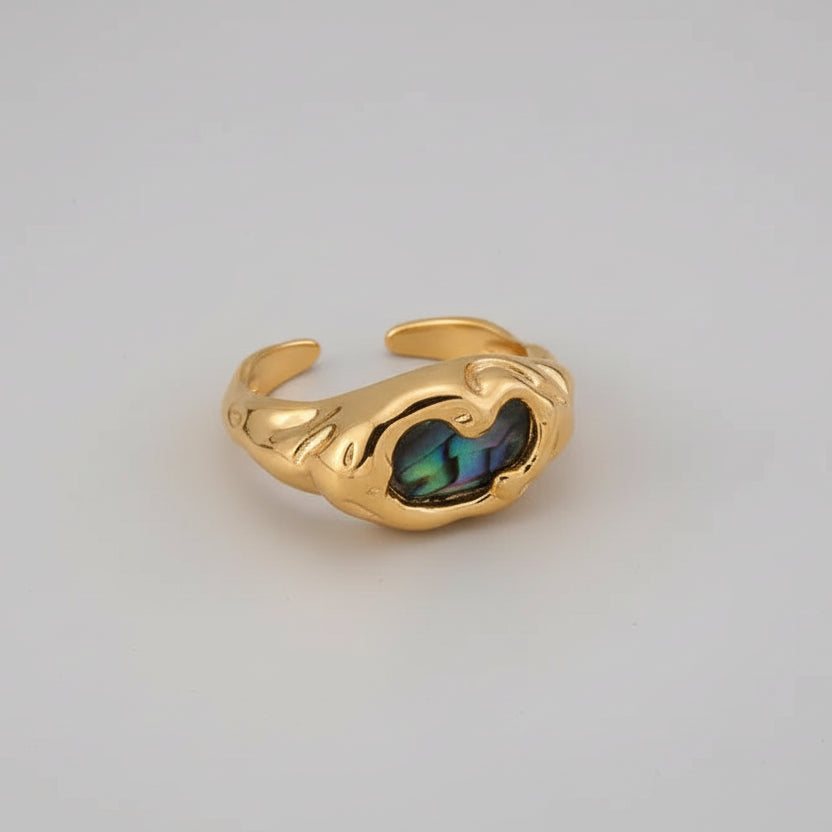 Gold ring with a black abalone gemstone on a white stone surface