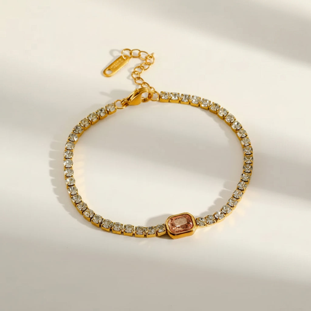 Gold bracelet with a central pink gemstone on a light background