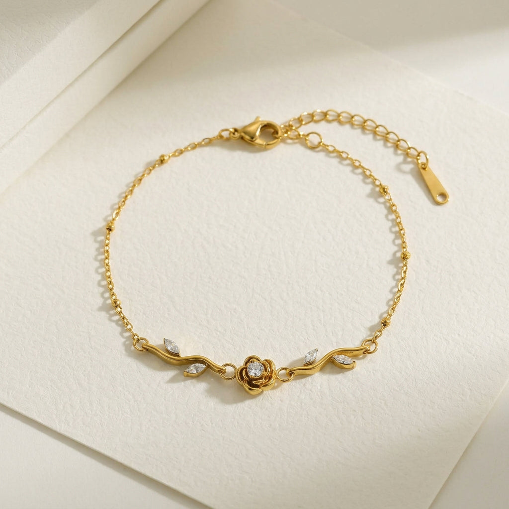 Gold chain bracelet with a central rose charm set with clear stones, leaf-shaped accents, and an adjustable clasp, displayed on a light textured surface with printed measurements and weight details.