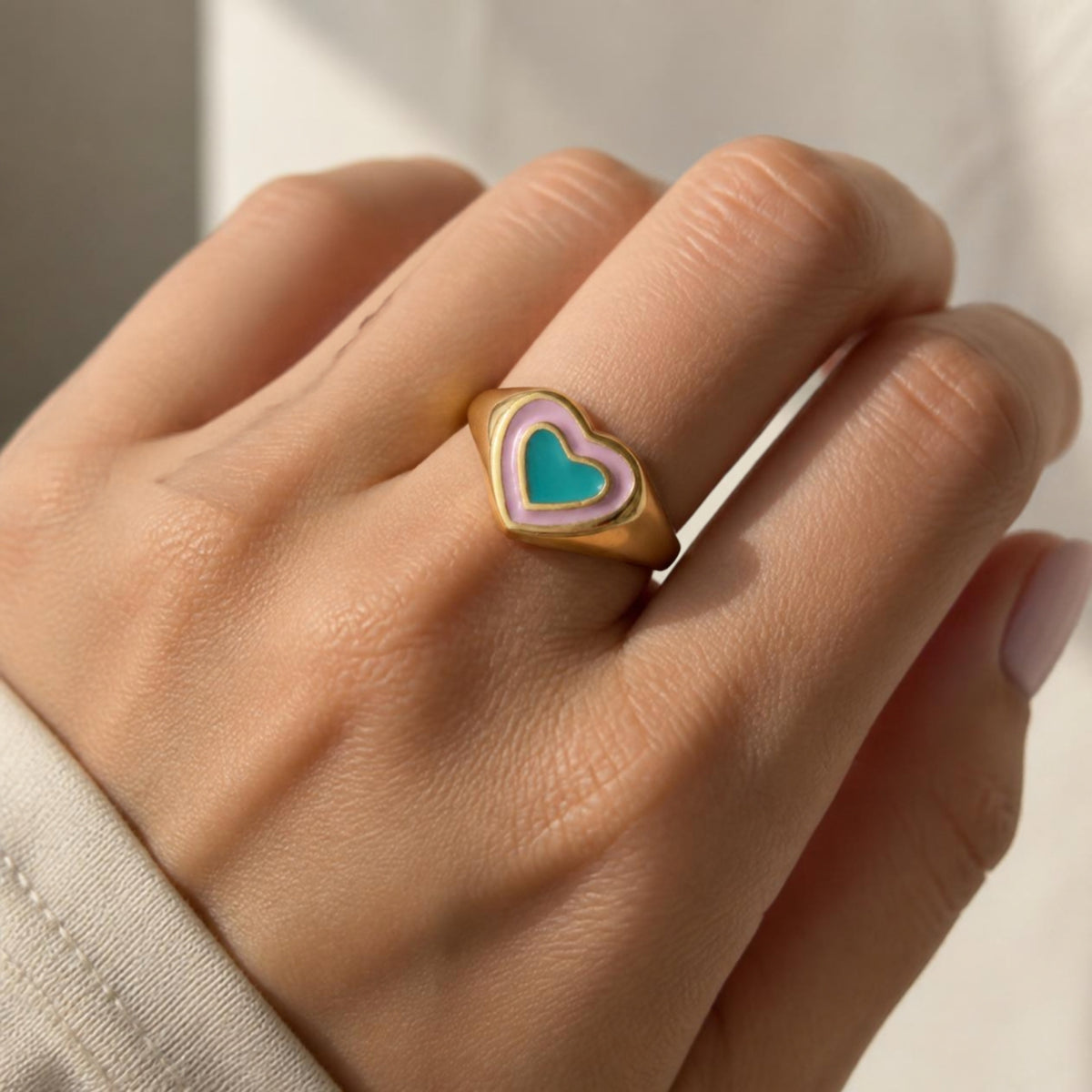 True Love Ring worn on finger, showing the turquoise heart bordered by a pink outline on a gold signet ring