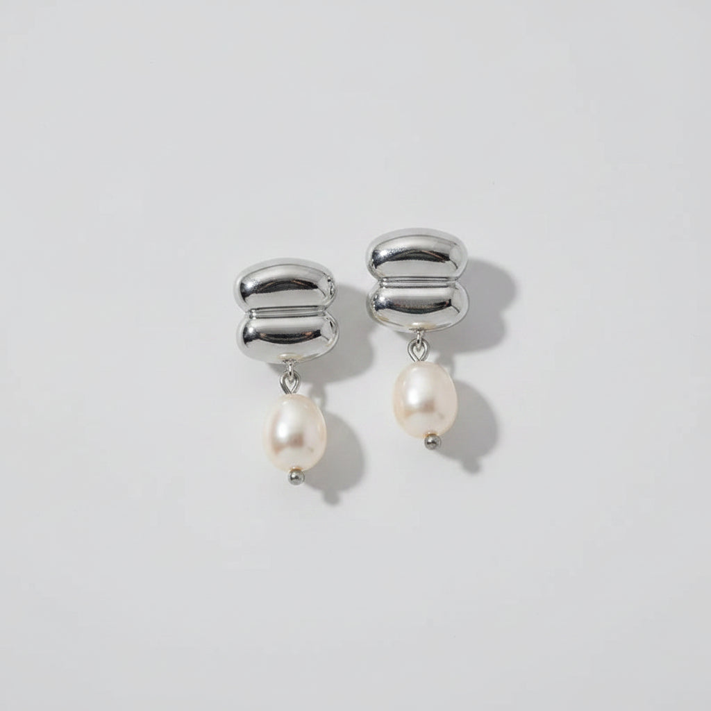 Silver earrings with pearls on a sandy background