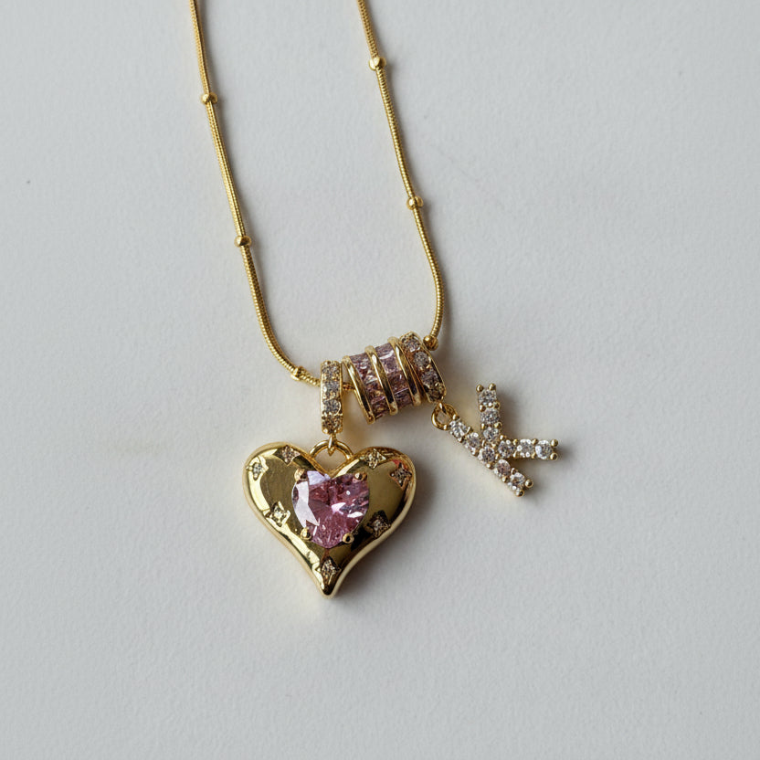 Gold necklace with heart pendant and 'K' charm on a light gray background