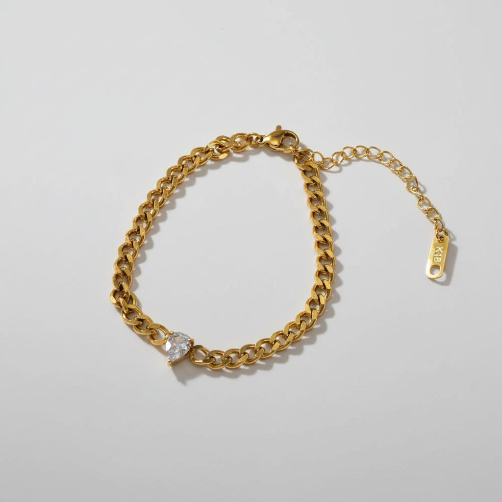 Gold chain bracelet with a pear-shaped charm on a beige background