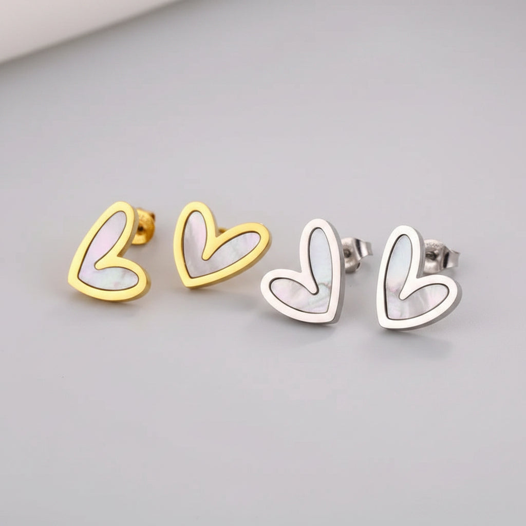 Pair of heart-shaped earrings, one gold and one silver, on a soft fabric background.