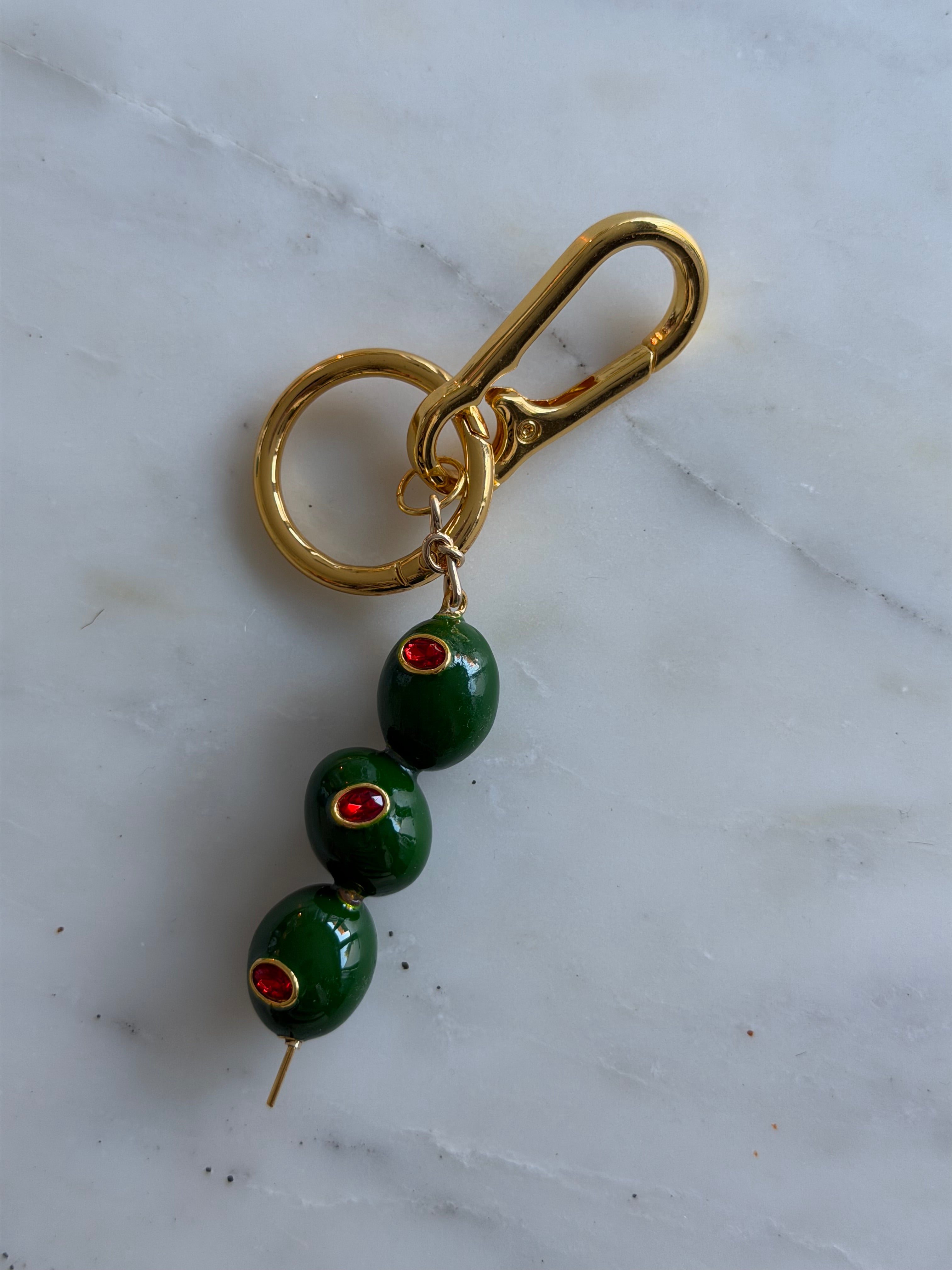 Gold keychain with green olives on a marble surface
