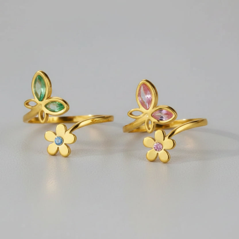 Gold butterfly and flower-shaped rings with gemstones on a beige background