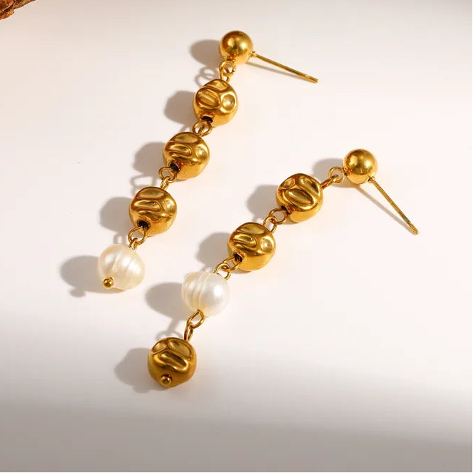 Gold and pearl earrings on a neutral background