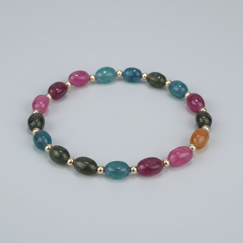 Multicolored beaded bracelet on a textured surface with text indicating size and material.