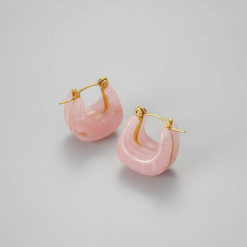 Pink hoop earrings with gold accents on a beige fabric background