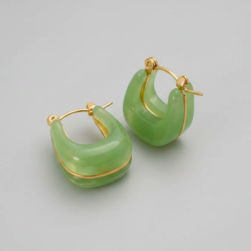 Green hoop earrings with gold accents on a beige fabric background