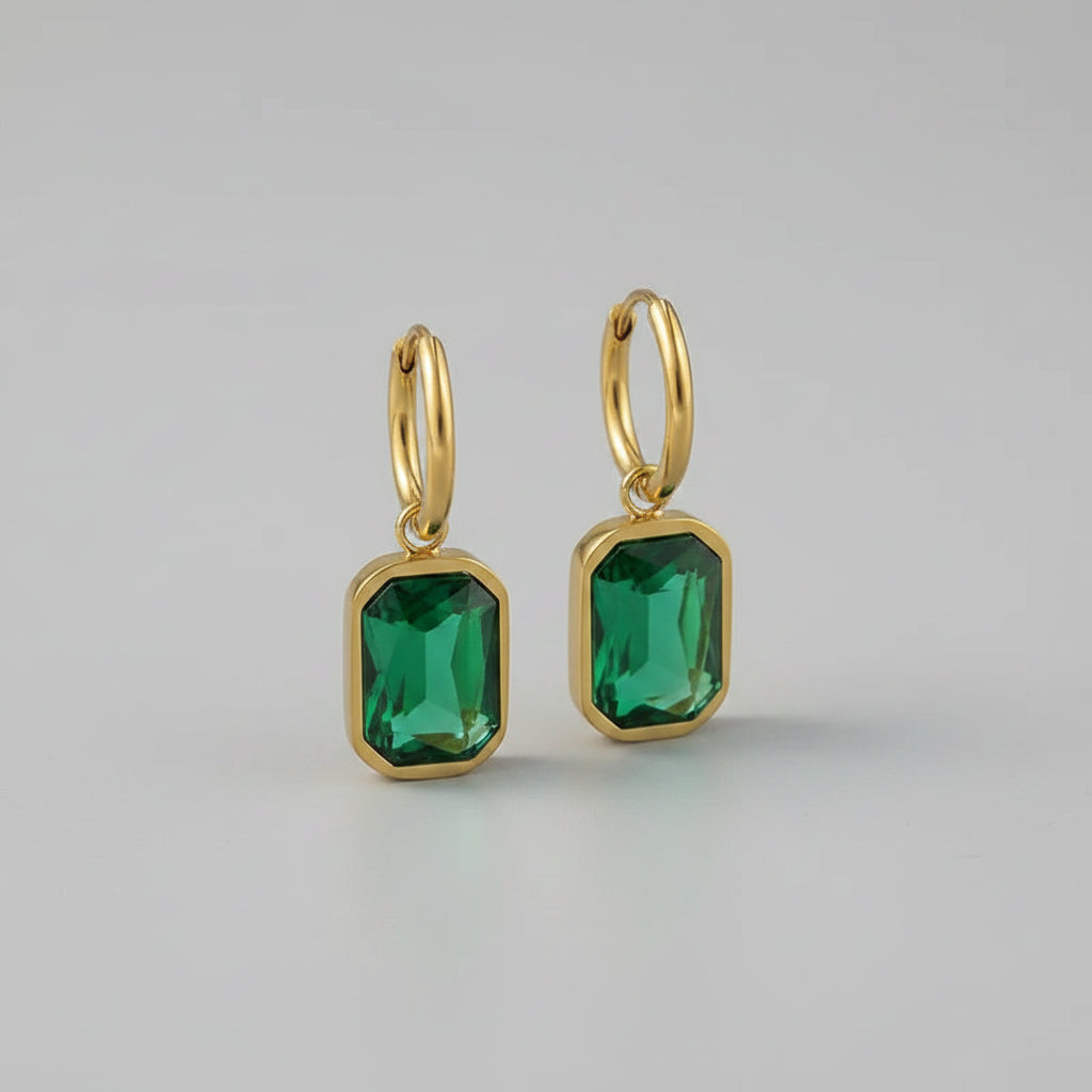 Gold hoop earrings with green gemstones on a beige surface