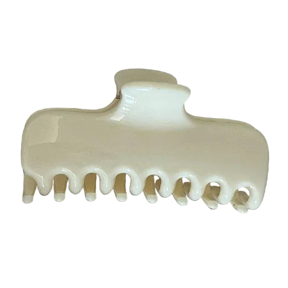 An off-white glossy hair claw clip placed on a textured beige linen fabric background.