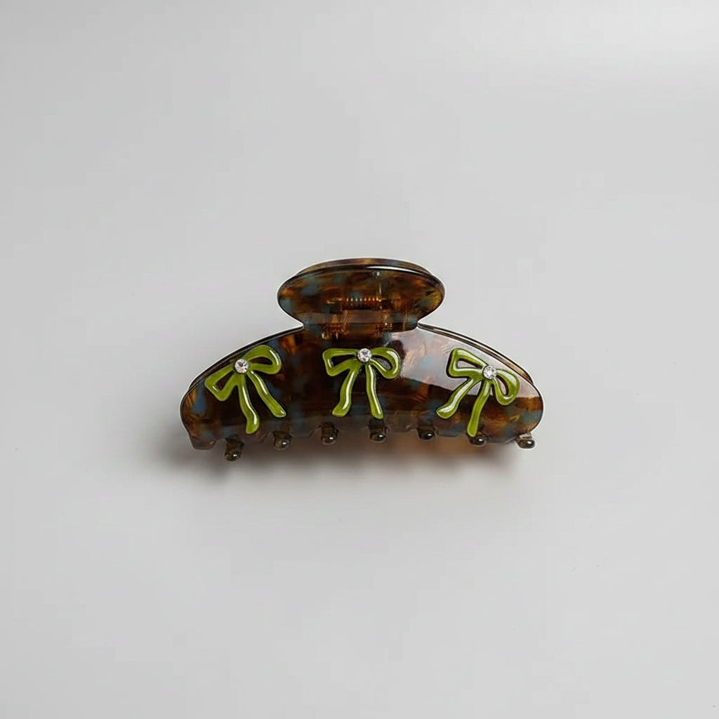 Tortoiseshell hair clips with green bows on a white fabric background