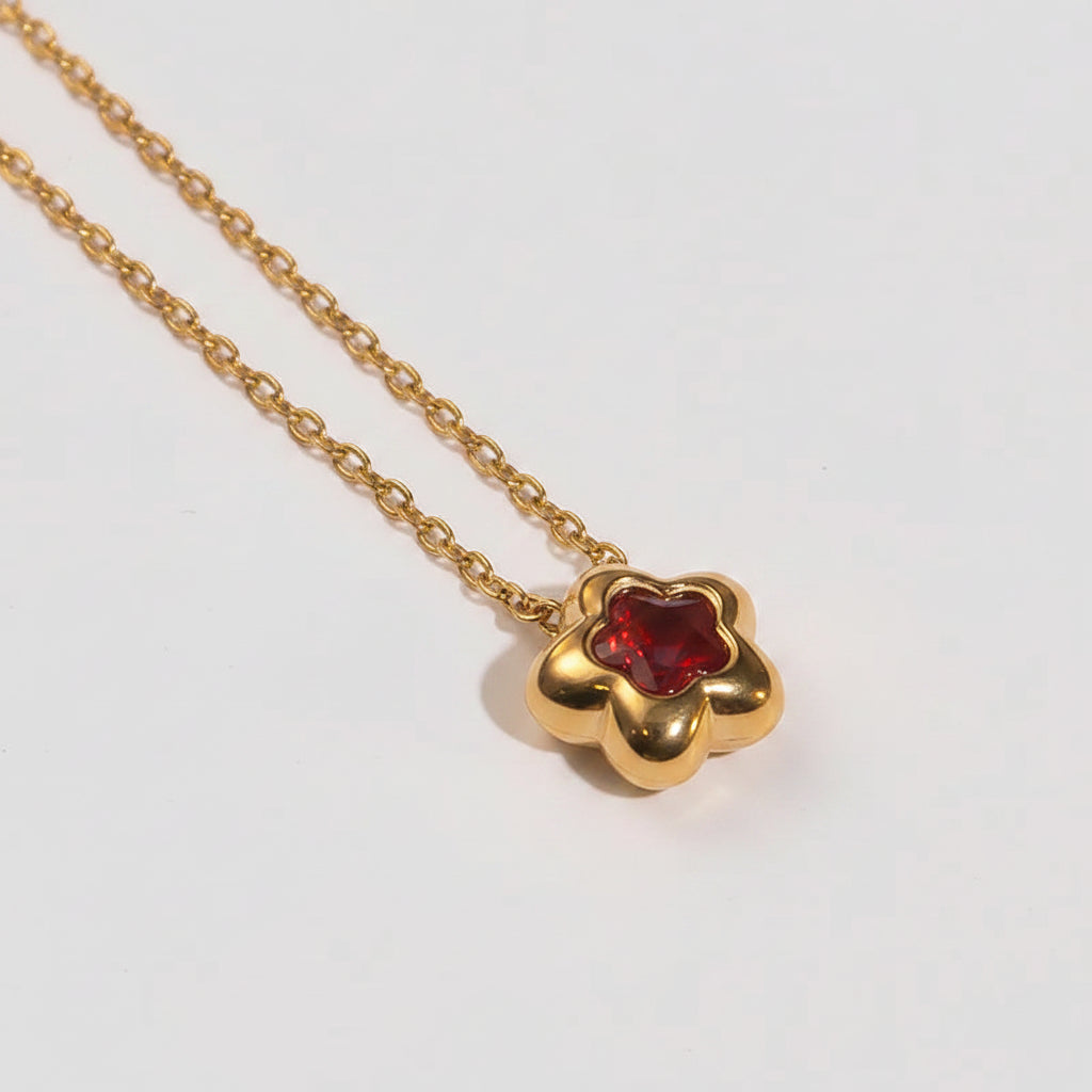 Gold necklace with a red flower pendant on a light beige background