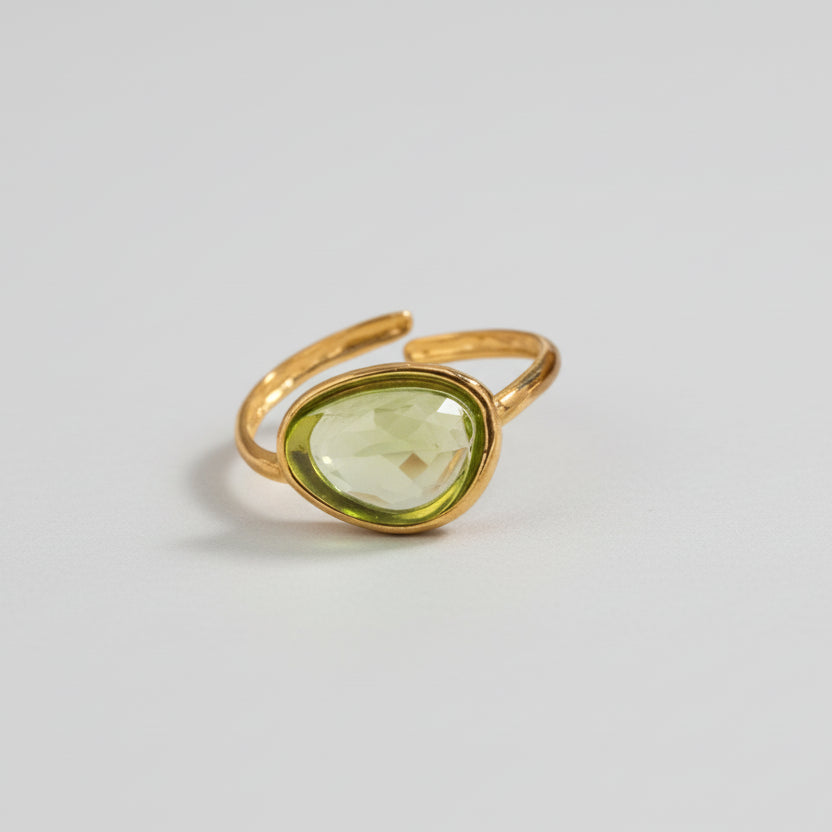 Gold ring with a green gemstone on a beige surface