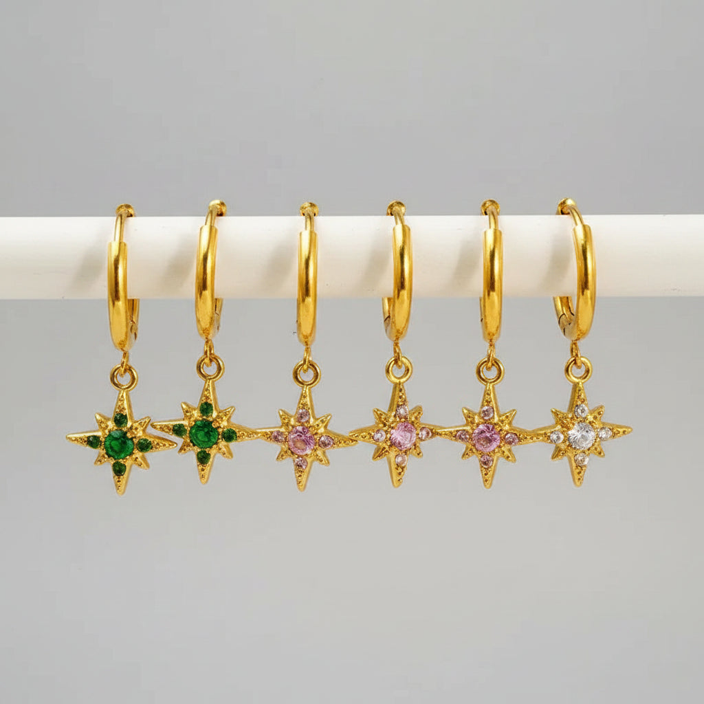 Gold hoop earrings with star-shaped charms on a wooden stick against a gold background