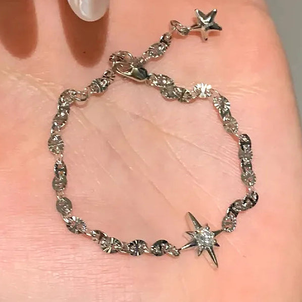 Silver bracelet with star charms on a hand against a neutral background