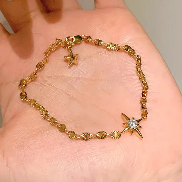 Gold bracelet with star designs on a hand against a neutral background